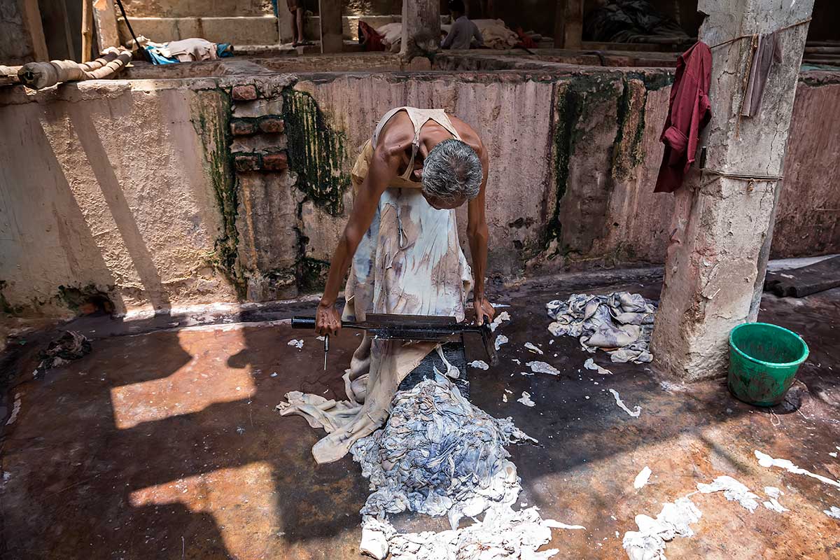 A man scrapes the inside of a cow skin to remove small parts to make it smoother. He uses a special designed sharp tool.