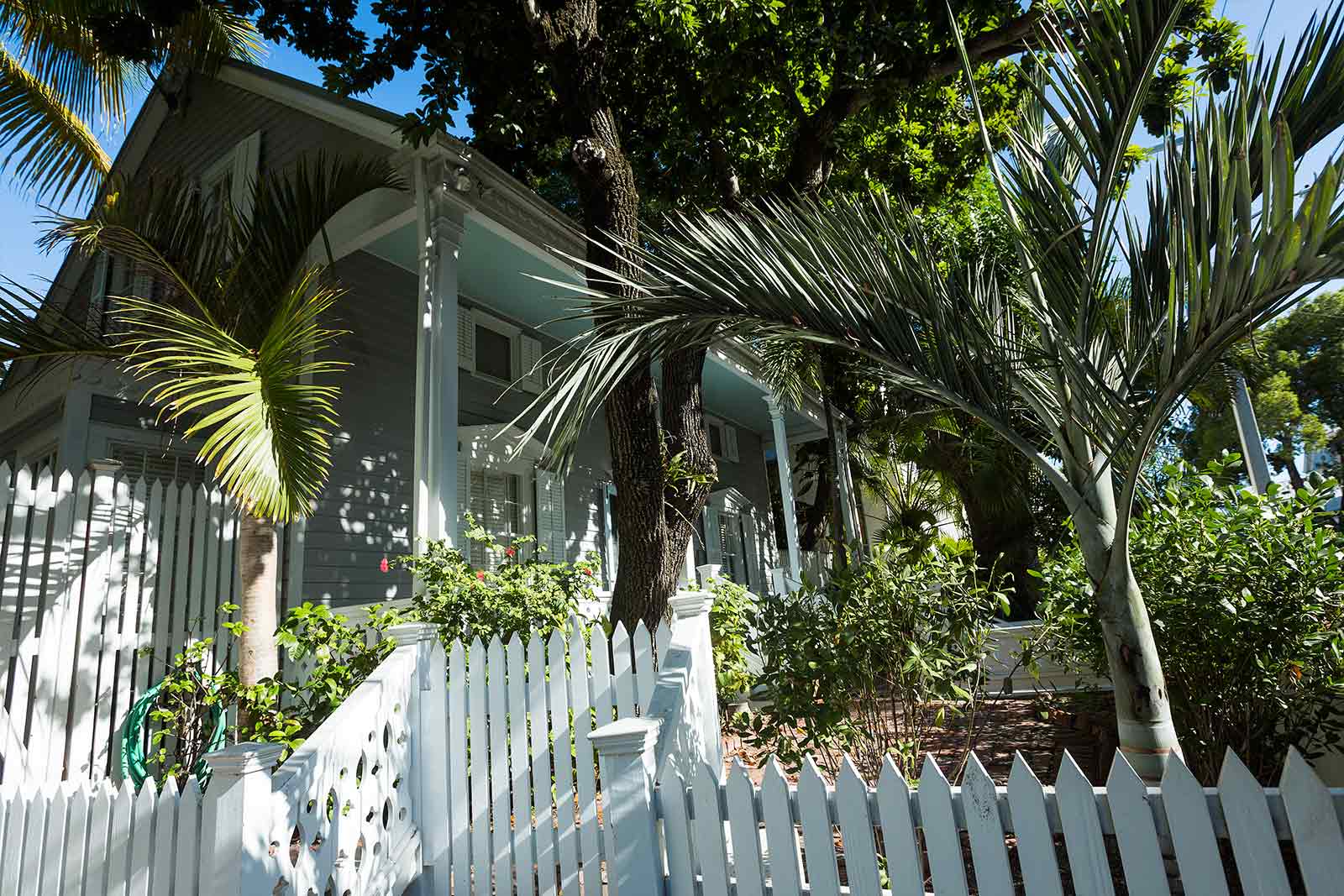 Key West houses are often surrounded by lathe-turned picket fences that wrap around the entire structure. Blooming bushes add a visual pop and fresh contrast to fancifully painted homes.